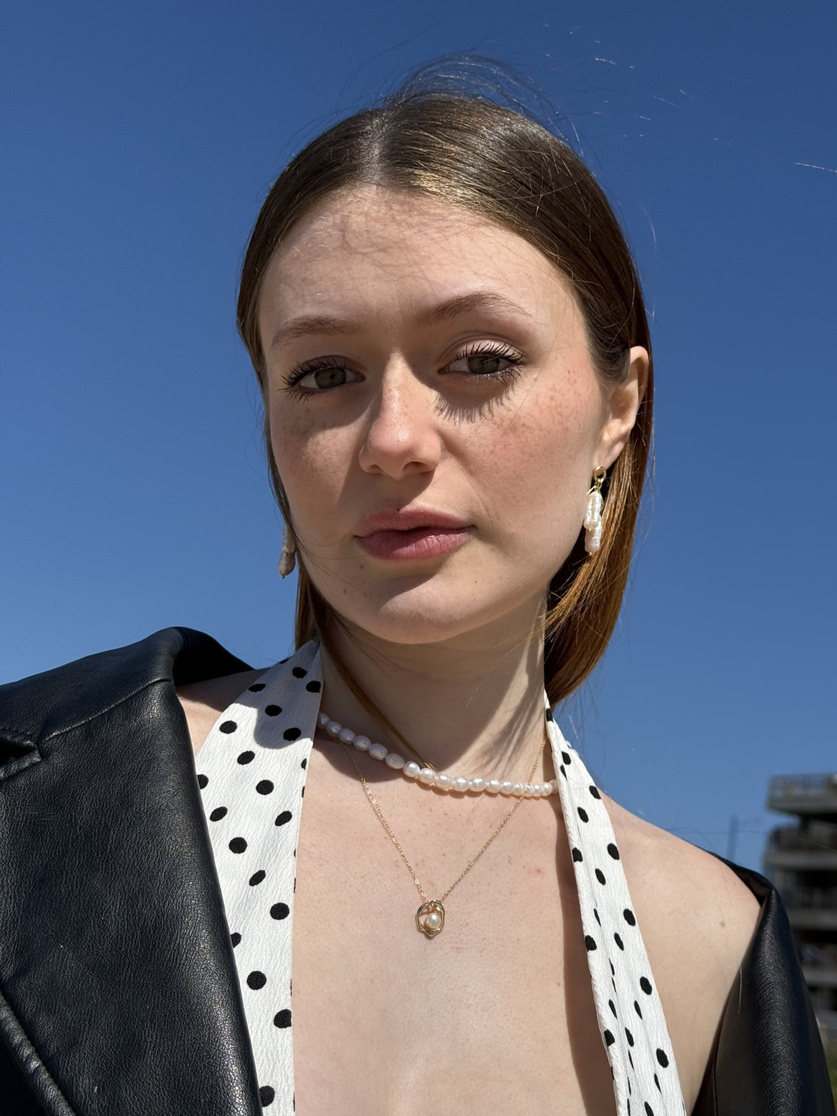 Pearl earrings and layered necklaces against a blue sky